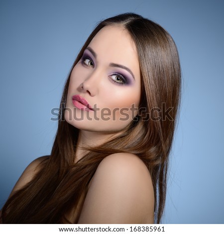 Beautiful girl. Natural beauty portrait. Young woman with beautiful healthy face and long brown hair looking at camera. Studio shot of attractive fresh girl over blue background.