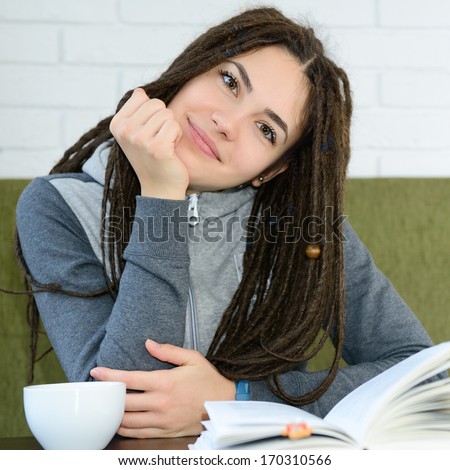 Young woman drinking coffee and reading book sitting indoor in urban cafe. Cafe city lifestyle. Casual portrait of teenager girl.
