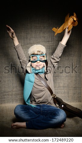 Little boy aviator dreaming and playing with wooden handmade toy plane over vintage canvas background
