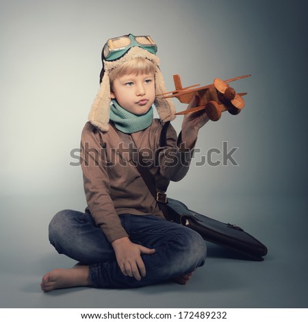 Little boy aviator dreaming and playing with wooden handmade toy plane, vintage toned