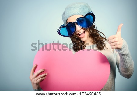 Cute attractive fashion young girl posing with funny big love glasses and pink heart with thumb up, toned