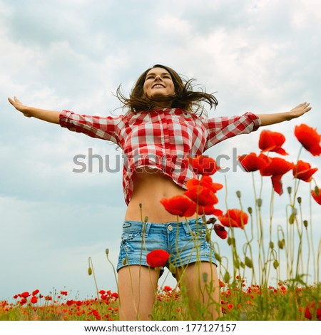 Young beautiful woman walking and dancing through a poppy field, summer outdoor.