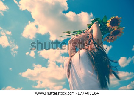 young beautiful woman enjoying summer, youth and freedom, holding sunflowers above head, against blue sky, toned