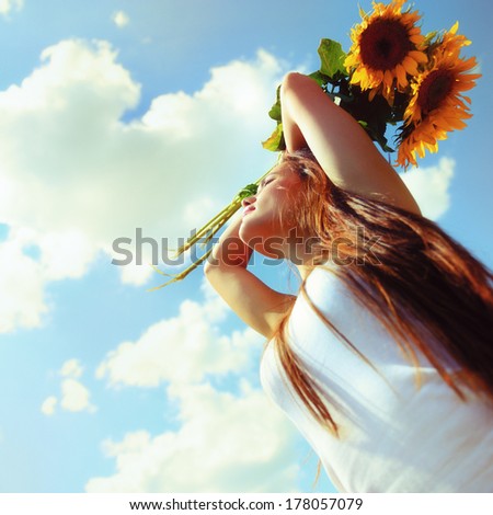 Young beautiful woman enjoying summer, youth and freedom, holding sunflowers above head, against blue sky, toned image
