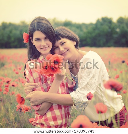Attractive middle-aged woman have fun on a poppy field with her, summer outdoor. Image toned.