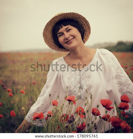 Cheerful attractive woman has fun on a poppy field, summer outdoor. Image toned.