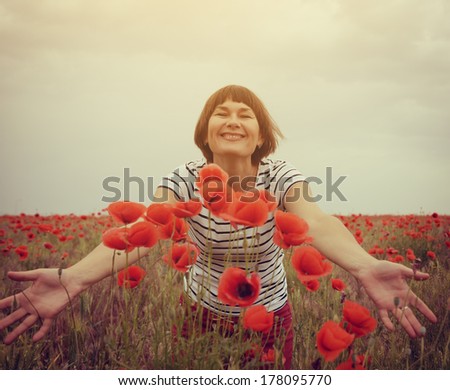 Cheerful attractive woman has fun on a poppy field, summer outdoor. Image toned.