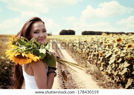 young beautiful woman enjoying summer, youth and freedom, holding sunflowers above head, against blue sky