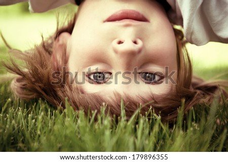Happy little boy standing upside down on green grass in spring park, toned