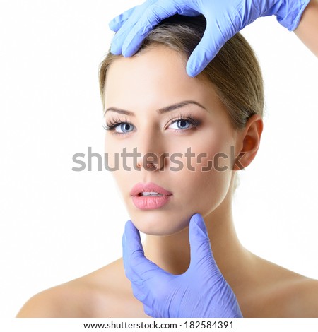 Beauty treatment of the young beautiful female face, doctor\'s hand in gloves touch face of beautiful young woman isolated on white