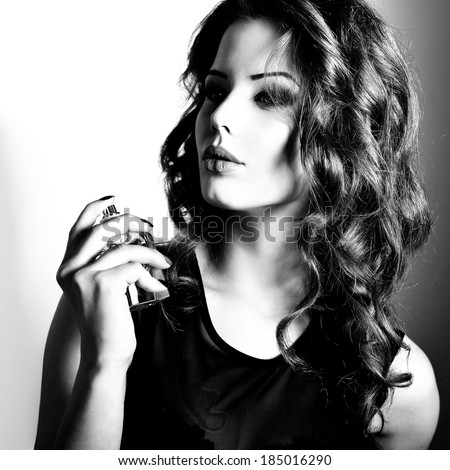Girl with perfume, young beautiful woman holding bottle of perfume and smelling aroma. Black and white.