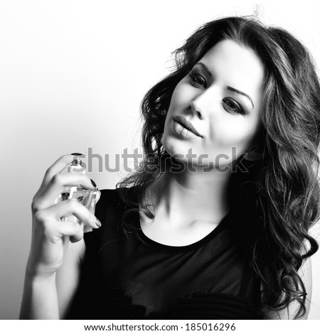 Girl with perfume, young beautiful woman holding bottle of perfume and smelling aroma, black and white.