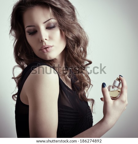 Girl with perfume, young beautiful woman holding bottle of perfume and smelling aroma, toned.