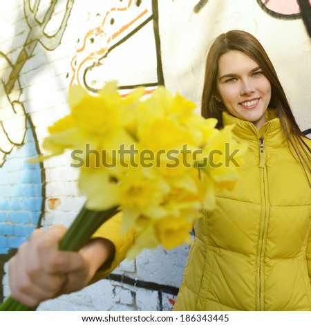 Happy attractive girl with yellow spring flowers over urban abstract graffiti wall