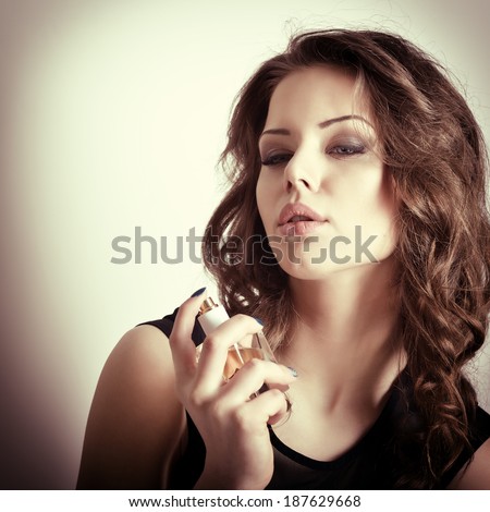 Girl with perfume, young beautiful woman holding bottle of perfume and smelling aroma, toned soft beige.