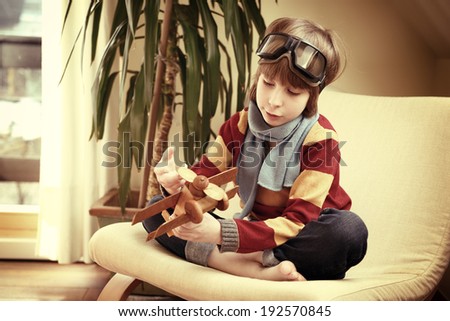 Little boy aviator dreaming and playing with wooden handmade toy plane at home, vintage toned