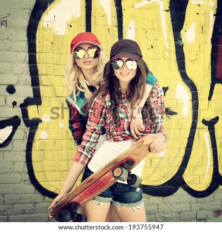 Two teen girl friends having fun together with skate board. Outdoors, urban lifestyle. Toned.