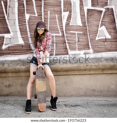 Portrait of beautiful teen girl standing on skateboard over wall with abstract graffiti art. Urban outdoors, teenager\'s lifestyle. Toned.