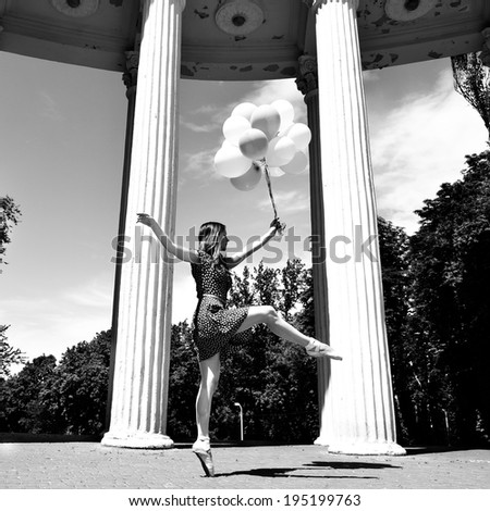 Attractive teen girl dancing outdoor in park against columns with balloons. Black and white.