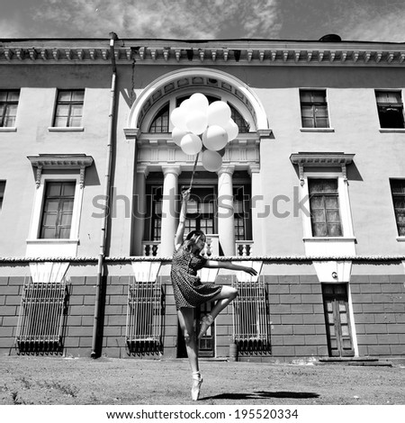 Attractive teen girl dancing with balloons outdoor against old building. Black and white.
