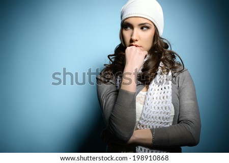 Cute attractive fashion young girl in warm clothes looking left at copyspace, over blue