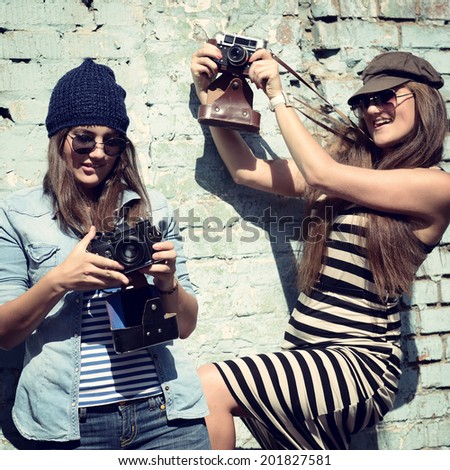 Urban girls have fun with vintage photo cameras outdoor near grunge wall, filtered