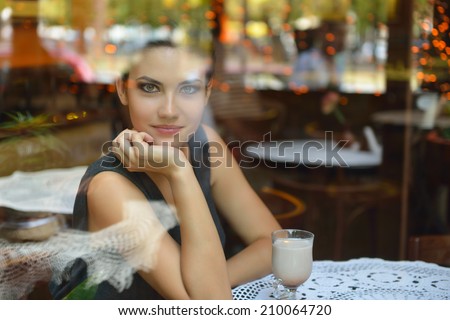 Young beautiful woman sitting in cafe, drinking coffee. Image toned, noise added.