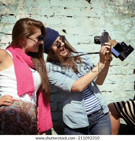 Urban girls have fun with vintage photo cameras outdoor near grunge wall, filtered