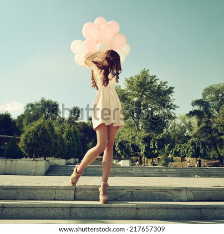 Fashion girl with air balloons steps on stairs, image toned.
