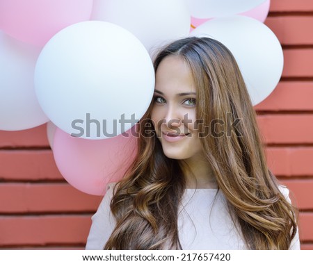 Happy young woman standing over red brick wall and holding pink and white balloons. Pleasure. Dreams. Image toned.