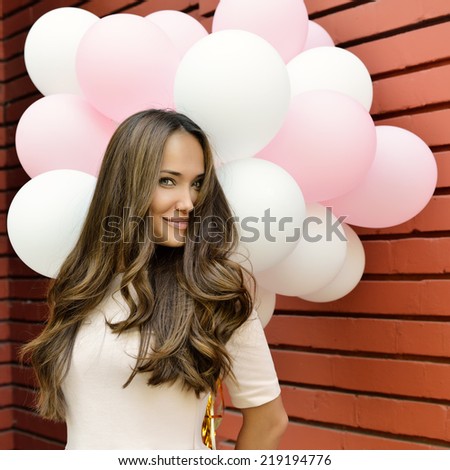 happy young woman standing over red brick wall and holding pink and white balloons, toned.