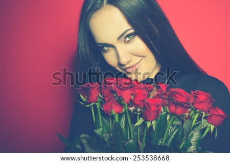 Beautiful Woman with Fresh Red Roses. Girl and Flowers over Red Background. Beauty Female Face. Happiness, Freshness, Beauty, Youth. Image Toned.