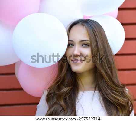 Happy young woman standing over red brick wall and holding pink and white balloons. Pleasure. Dreams.