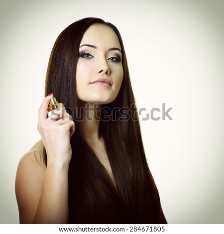 Girl with perfume, young beautiful woman holding bottle of perfume and smelling aroma, toned soft beige and noise added