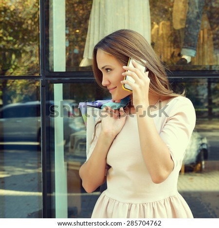 Beautiful young fashion woman with shopping bags near shop window calling smart phone