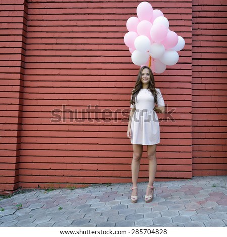 Happy young woman standing over red brick wall and holding pink and white balloons. Pleasure. Dreams. Toned.
