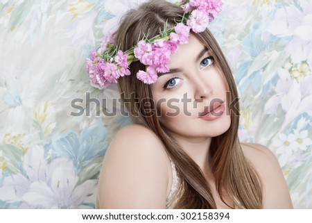 Young woman with beautiful healthy face and long fair hair in garland of pink flowers. Studio shot of attractive girl looking at camera over white background. High key.