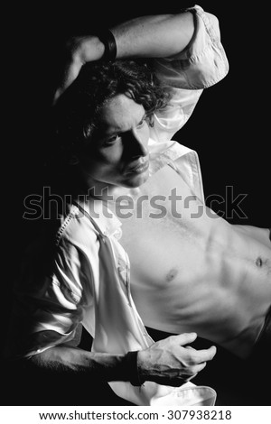 Portrait of young handsome man with open white shirt and rich curly hair over black background. Black and white.