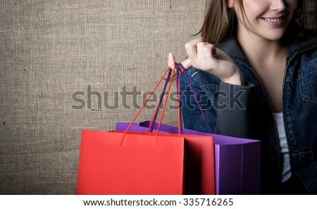 Young happy smiling woman holding red and purple shopping bags over canvas, image toned.