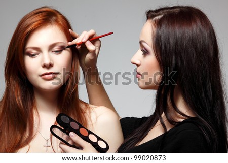 Portrait of beautiful young redheaded woman with esthetician making makeup eye shadow