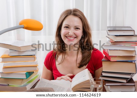 Studying happy young woman reading her book for school. Woman seating at the table with books. Smiling female student is studding up. Teenager girl with lots of books study and read