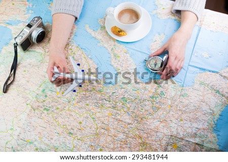 Destination points. A woman sitting at table with a map, airplane, compass and camera and visualises his desire to travel.  Top view. Globetrotter coffee break for trip dreams.