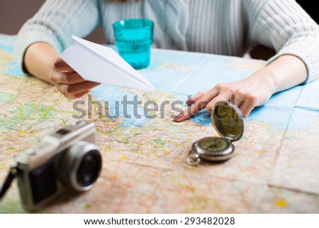 holidays and tourism concept - women with tourist map planning travel destination sitting at table with map with paper airplane, compass, camera and visualises desire to travel Shallow depth of field