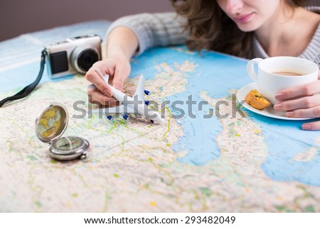Globetrotter coffee break for trip dreams. A woman sitting at table with a map with a paper airplane, compass and camera and visualises his desire to travel. Shallow depth of field