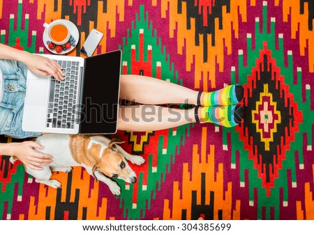 girl with a dog at the computer sitting on the floor with a cup of herbal tea. Beautiful national rug home comfortable relaxed atmosphere. Top view. Beautiful fit slim legs