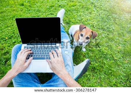 Modern life working outside. Man with dog using laptop sitting on the green grass in the park