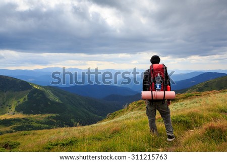 Man traveler hiking in the mountains with a large tourist backpack. Standing back. Admiring the beautiful scenery of Ukrainian Carpathian Mountains. Dramatic cloudy sky.