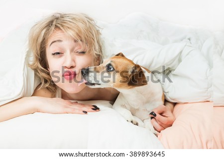 Happy funny morning mood. fooling around with pet on bed. Relaxed sleepy Woman and dog kiss on the pillow and linen