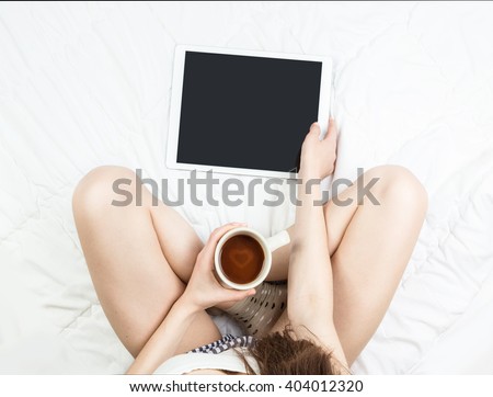 Web site visiting on the bed with tablet pc. Young girl legs on the bed. Holding cup of love coffee coca. Relaxed lazy online shopping.  top view