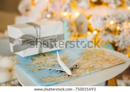 Travel present for New Year. Toy airplane with map, present box and Christmas tree. Cozy lights decoration. Happy Xmas!